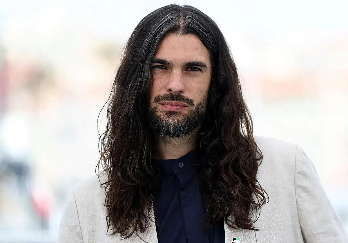 Oliver Laxe, director de cine, con su larga melena y barba, viste una chaqueta clara.
