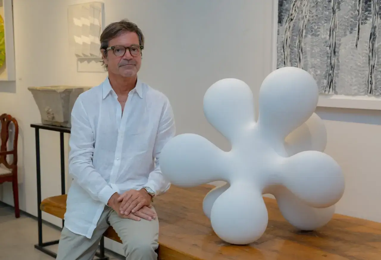Eduardo Pérez-Cabrero, con su pareja, posa junto a una escultura abstracta blanca en una galería de arte.