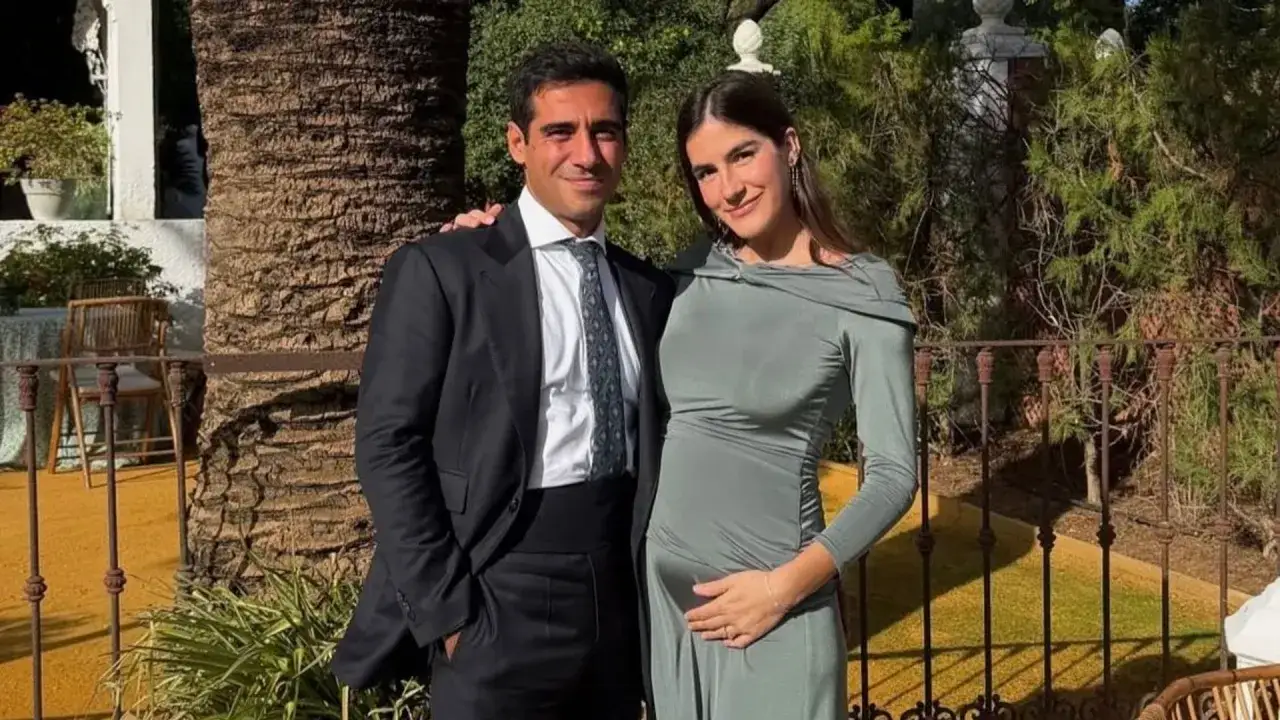 Pareja sonriente, &eacute;l con traje, ella con vestido verde y mano en el vientre. Blanca Llandres, radiante, espera un beb&eacute;.