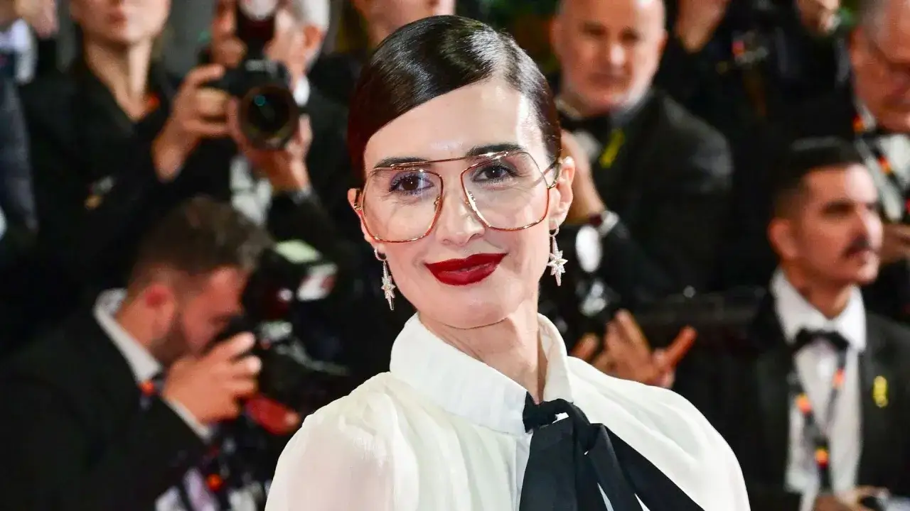 Jone Laspiur, con gafas llamativas y labios rojos, sonríe ante los fotógrafos.