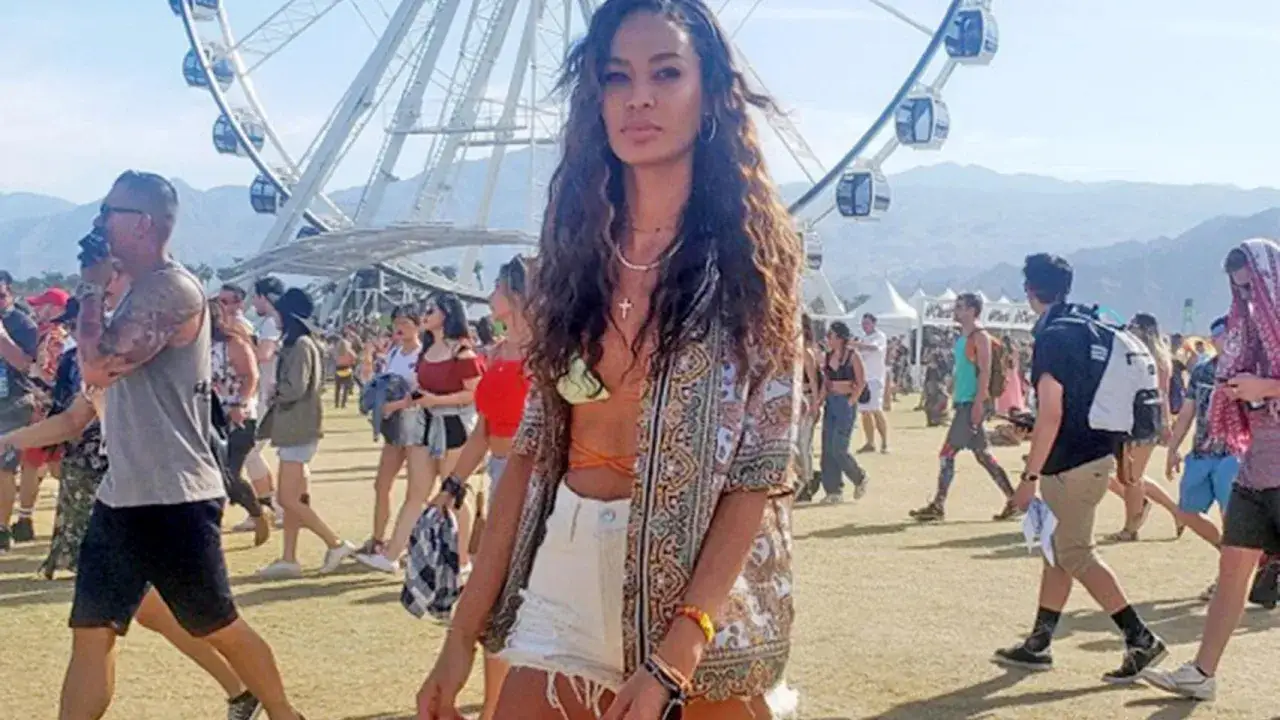 Una mujer posa en un festival de verano, con una noria y una multitud al fondo.