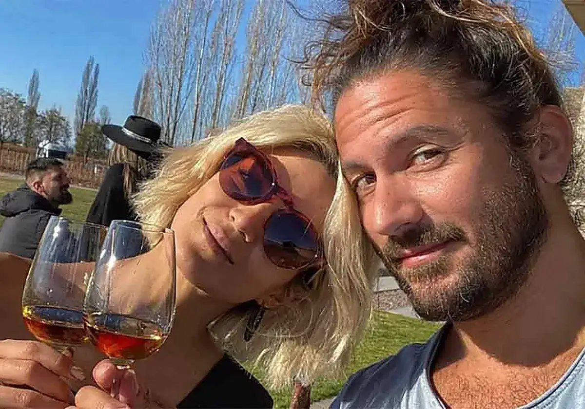 Pareja feliz en un día soleado, brindando con copas de vino. El lago y los árboles crean un fondo idílico.