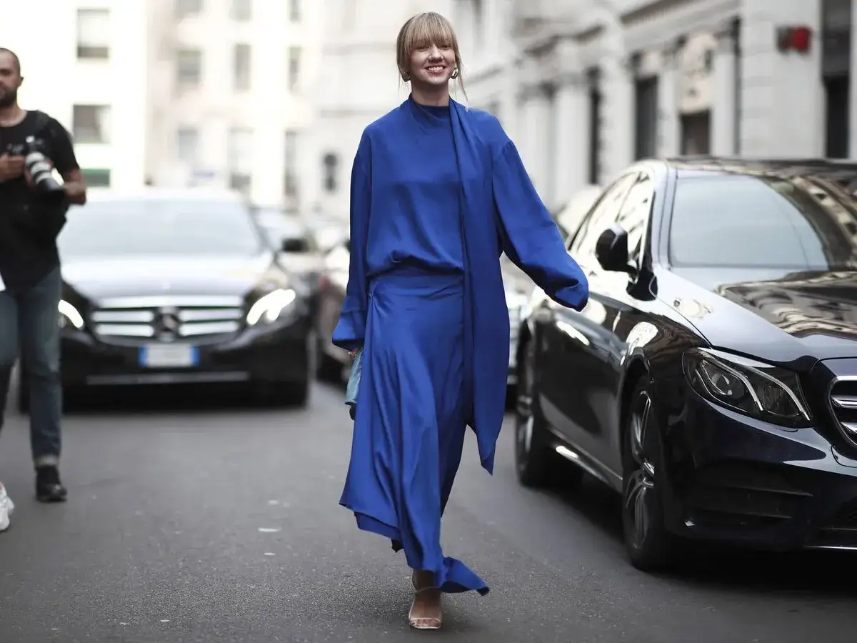 Mujer sonriente camina por la calle con un elegante vestido azul el&eacute;ctrico.