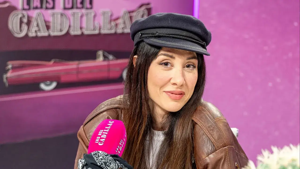 Natalia Ferviu sonríe con una gorra y chaqueta de cuero, con un fondo rosa y un Cadillac rojo.