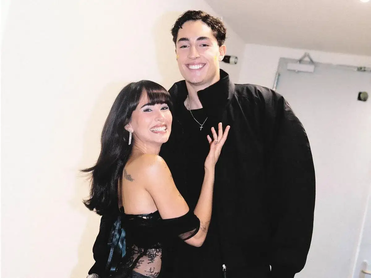 Aitana y su novio, ambos sonriendo, ella con un vestido negro y él con chaqueta negra.