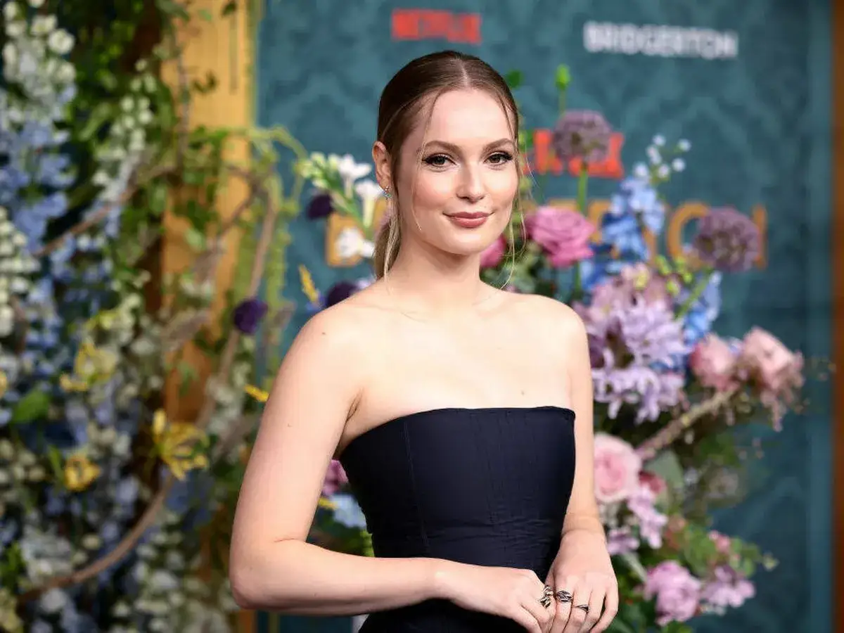 Hannah Dodd sonríe con un vestido negro sin tirantes, rodeada de flores vibrantes y el logo de Bridgerton.