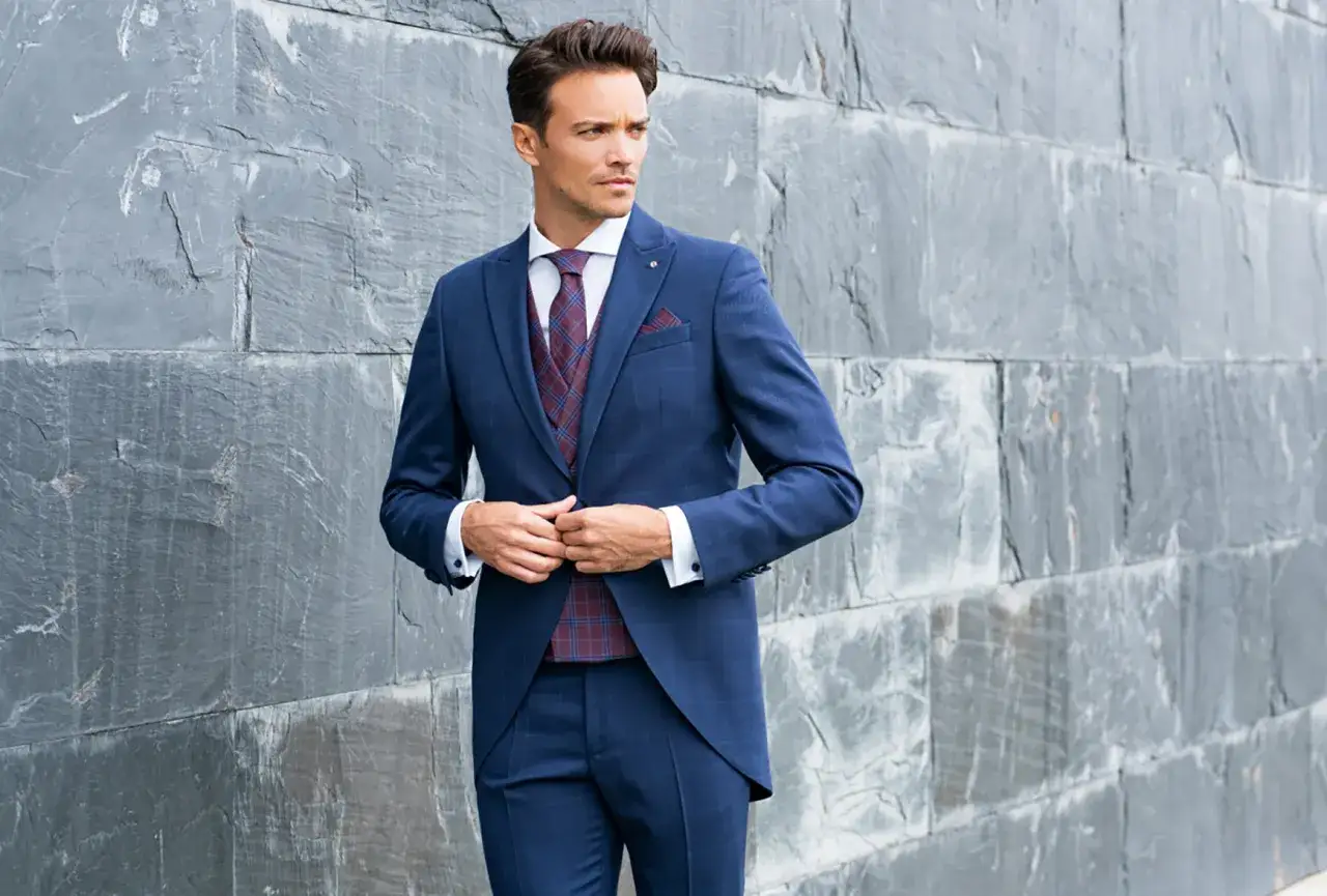 Elegante outfit boda hombre: traje azul a cuadros, chaleco a juego, corbata burdeos y pañuelo.