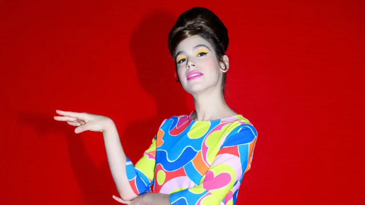 Cosima Ruiz de la Prada, con un peinado voluminoso y maquillaje vibrante, posa con un vestido de estampado psicod&eacute;lico sobre fondo rojo.