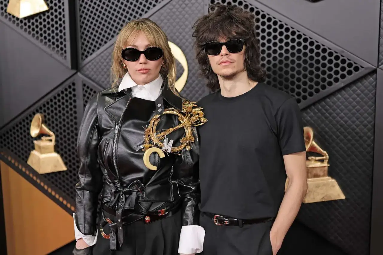 Maxx Morando y su pareja, luciendo gafas de sol, posan ante un fondo de los Grammy.