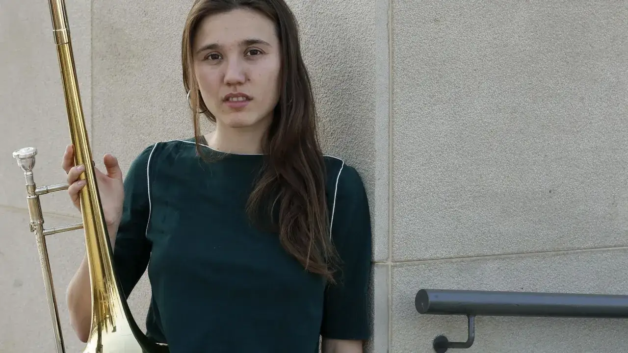 Rita Payés, con su trombón dorado, posa con una mirada serena junto a una pared texturizada.