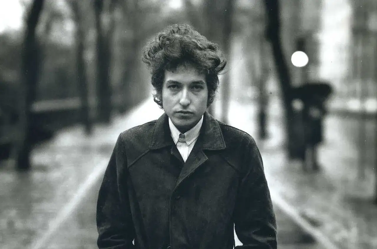 Retrato icónico de Bob Dylan, capturado por Richard Avedon. El joven músico mira fijamente a la cámara, con su característico cabello revuelto y un abrigo oscuro.