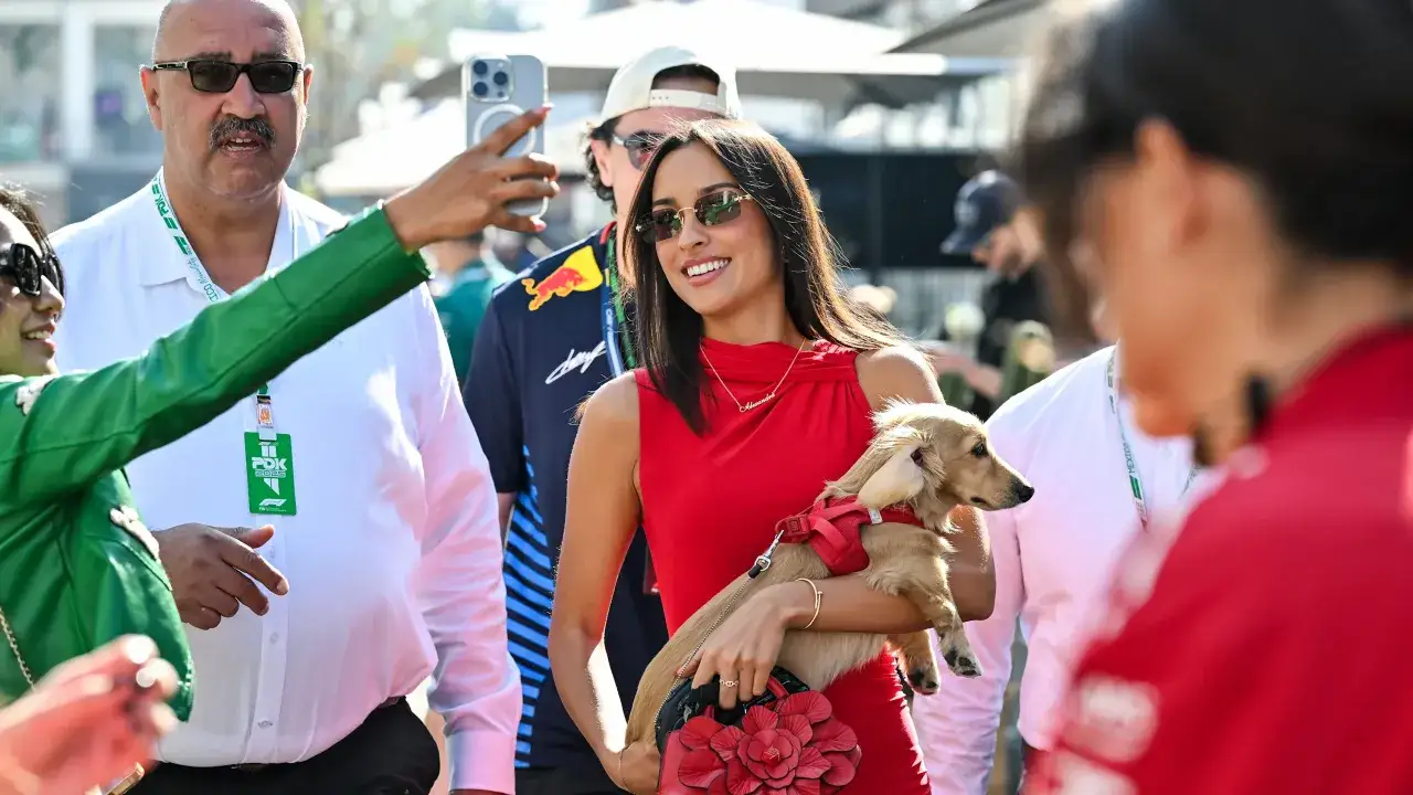 La novia de Charles Leclerc, con un vestido rojo y un perro salchicha, sonr&iacute;e mientras alguien toma una foto.