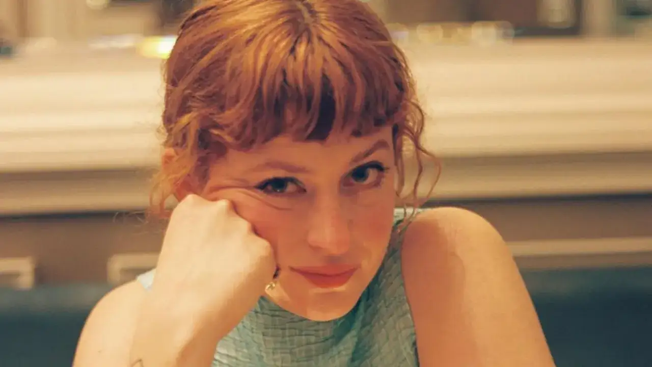Chloe Wallace, con su cabello rojizo y una mirada pensativa, apoya su mejilla en la mano.