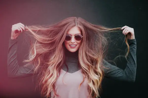 Chica sonriente con pelo largo y ondulado, mostrando cómo hidratar el pelo para un brillo radiante.
