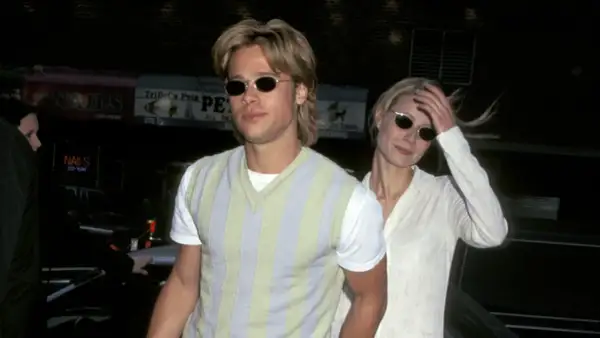 Brad Pitt joven con gafas de sol y un suéter a rayas, junto a una mujer rubia.