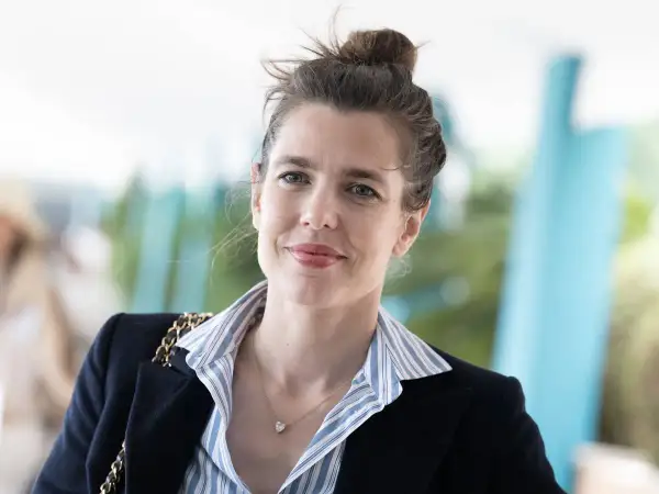 Carlota Casiraghi sonríe con su cabello recogido en un moño, luciendo un blazer oscuro y un collar con un colgante en forma de corazón.