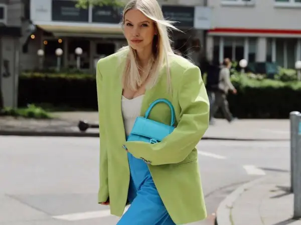 Mujer con blazer verde lima y pantalones azul eléctrico. Su bolso turquesa complementa perfectamente el conjunto, demostrando cómo el **verde y azul combinan** a la perfección.