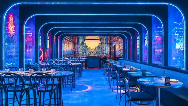 Un restaurante futurista con luces de neón azules y arte mural. Mesas puestas para cenar, quizás para disfrutar de una beata pasta bajo las estrellas.