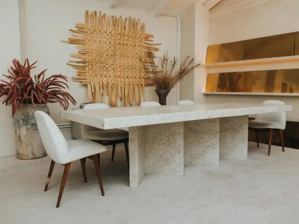 Comedor con mesa de terrazo y sillas tapizadas, arte de pared tejido y jarrones con flores secas. Un ambiente de lujo silencioso.
