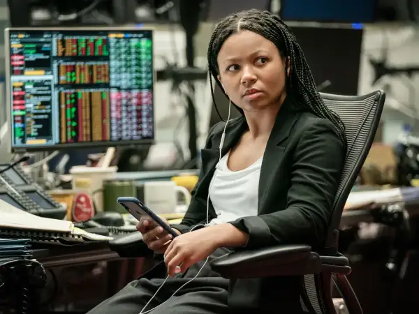 Myha'la Herrold, con auriculares, revisa su teléfono en una oficina con pantallas de datos financieros.