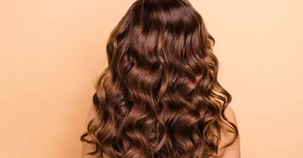 Cabello castaño con ondas naturales, un look de permanente ondulada que irradia brillo y movimiento.