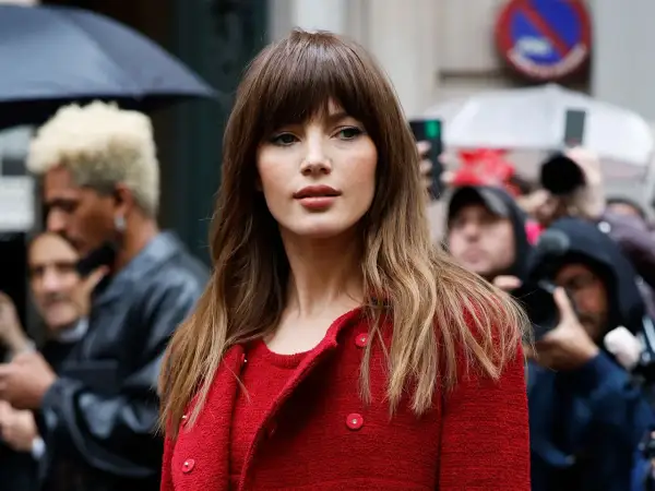 Mujer con flequillo y cabello castaño ondulado, luciendo un abrigo rojo. Un adelanto de los cortes de pelo 2026 mujer.
