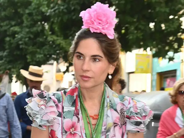 Lourdes Montes luce un vestido floral con volantes y una gran flor rosa en el pelo, adornada con un collar verde.