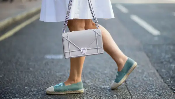 Piernas con un outfit veraniego, falda blanca y un bolso gris, completado con unas cómodas alpargatas de tela azul.